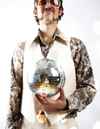 Instagram style portrait of a retro man in a 1970s leisure suit and sunglasses holding a disco ball - mirror ball